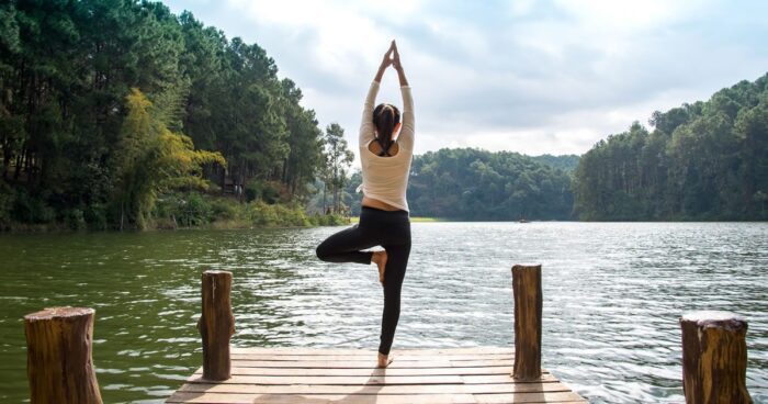 A woman practicing yoga on a wooden dock overlooking a serene lake surrounded by trees