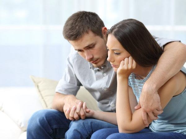 A man and woman sitting holding hands, looking worried