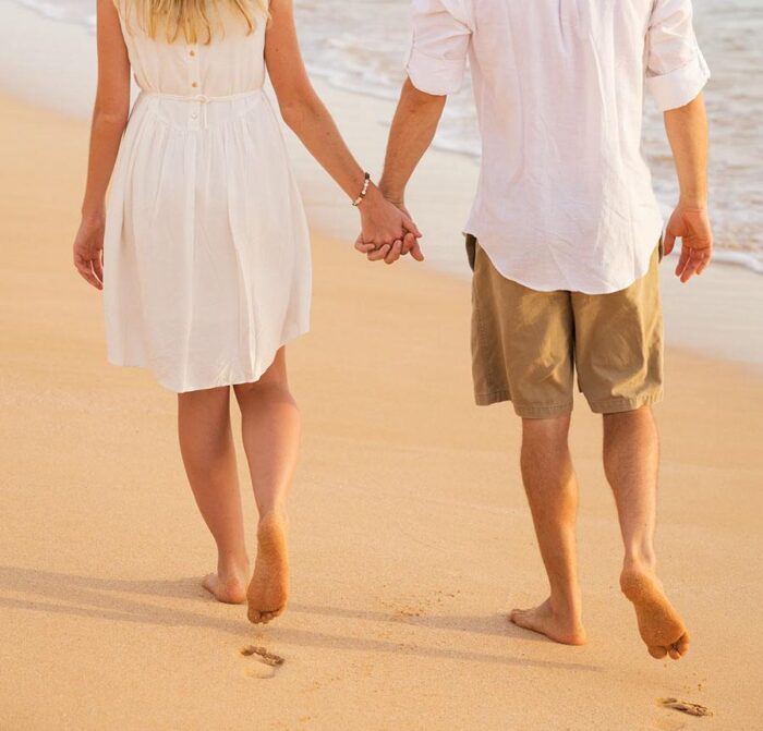 Man and woman holding hands walking on beach