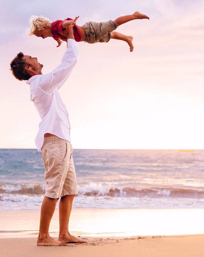 Man swinging child on beach