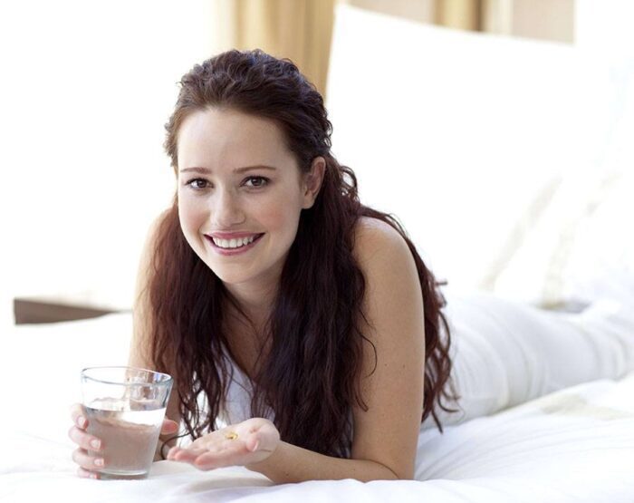 Woman taking folic acid with water.